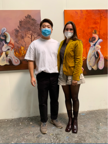 Fair Director Nicole Garton with artist Jay Chung in his studio, standing in front of 2 paintings